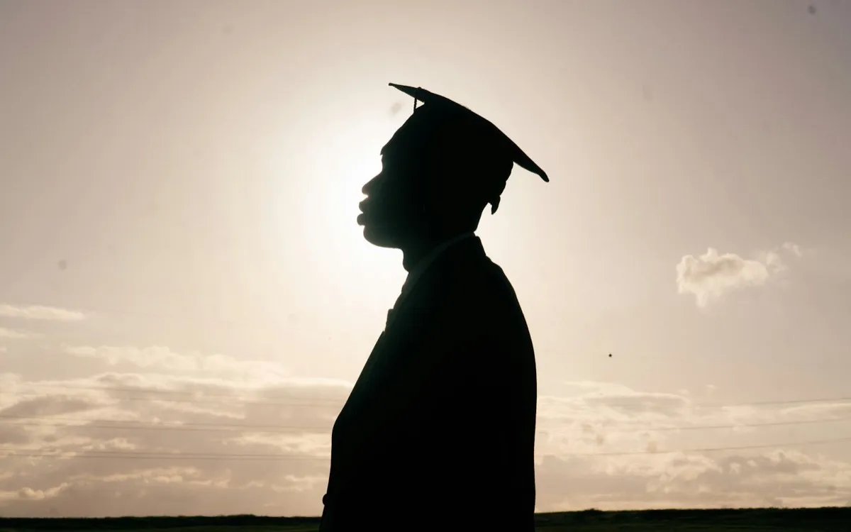 Silhouette of a graduate wearing a mortarboard cap against the evening sky